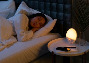 Mujer durmiendo plácidamente en una cama con ropa de cama suave y luz tenue, ambiente de descanso nocturno