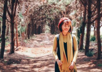 Mujer caminando sola por un sendero entre árboles, sonriente y disfrutando de la naturaleza al aire libre