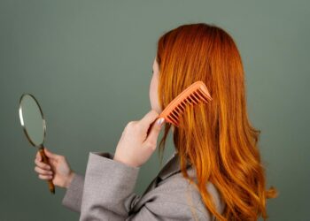 Mujer cepillando su cabello frente al espejo, cuidado capilar para frenar la caída del cabello