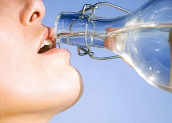 Mujer bebiendo agua de una botella, concepto de hidratación y hábitos saludables