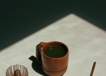 Taza de té verde recién preparado sobre una mesa de madera junto a hojas de té