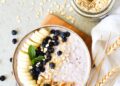 Bol de desayuno saludable con copos de avena, plátano, arándanos y nueces sobre una mesa clara