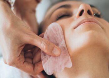 Masaje facial con piedra gua sha deslizándose sobre la mejilla de una mujer