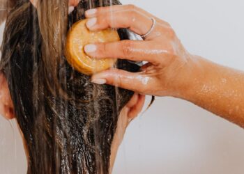 Mujer lavándose el pelo en la ducha para eliminar la caspa con un champú adecuado