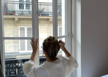 Mujer abriendo la ventana por la mañana durante la vuelta a la rutina tras las vacaciones