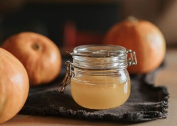 Frasco de vinagre de manzana para el pelo junto a manzanas frescas sobre una superficie clara