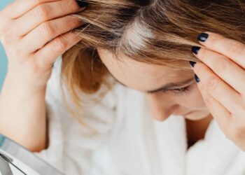 Mujer observando sus primeras canas en el espejo del baño