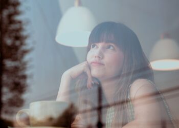 Mujer pensativa reflexionando sobre el síndrome del impostor junto a una ventana