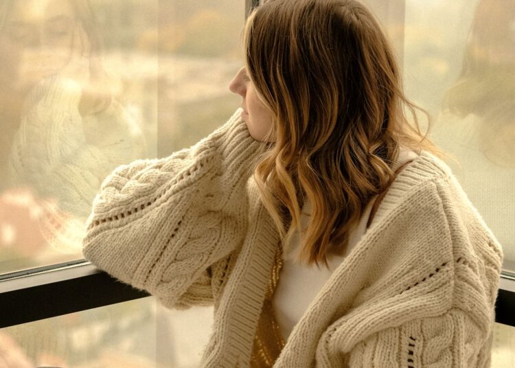 Mujer con una taza de té junto a la ventana afrontando el bajón de otoño