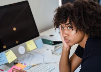 Mujer agotada por la carga mental sentada ante su escritorio con papeles y notas